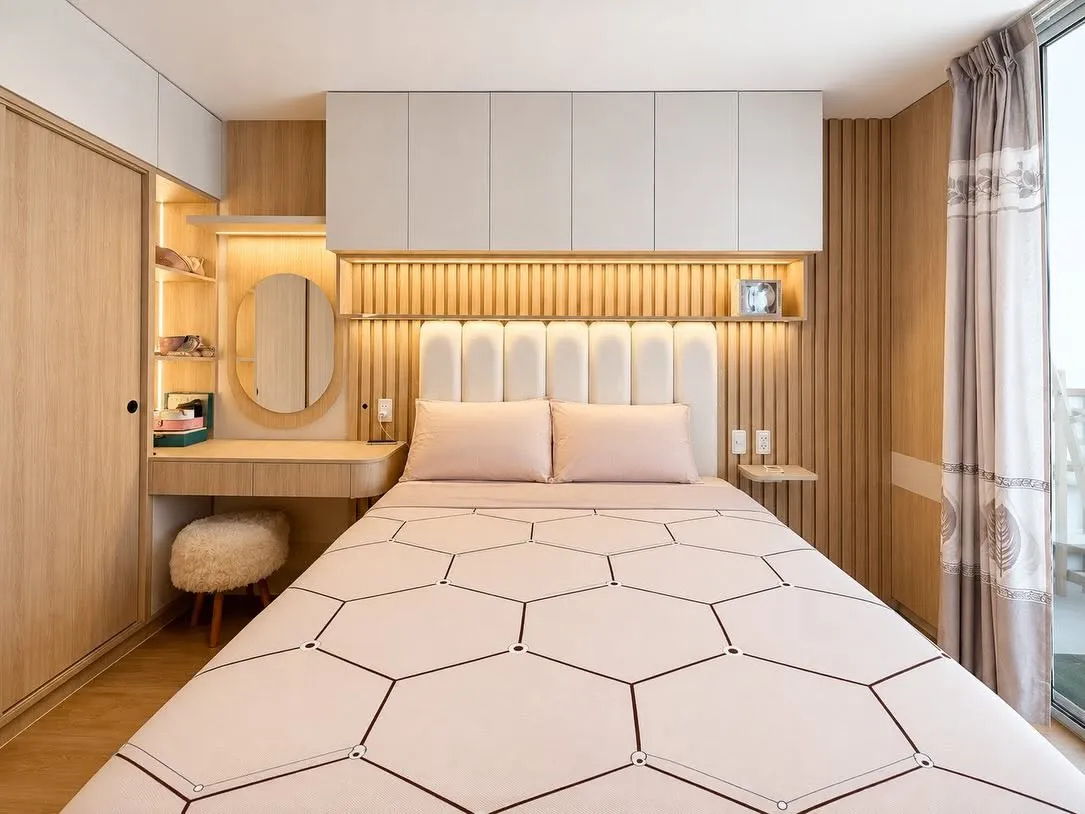 Dormitorio con cabecera tapizada acanalada en beige, paneles de listones de roble y cove de luz LED cálida sobre la cama
