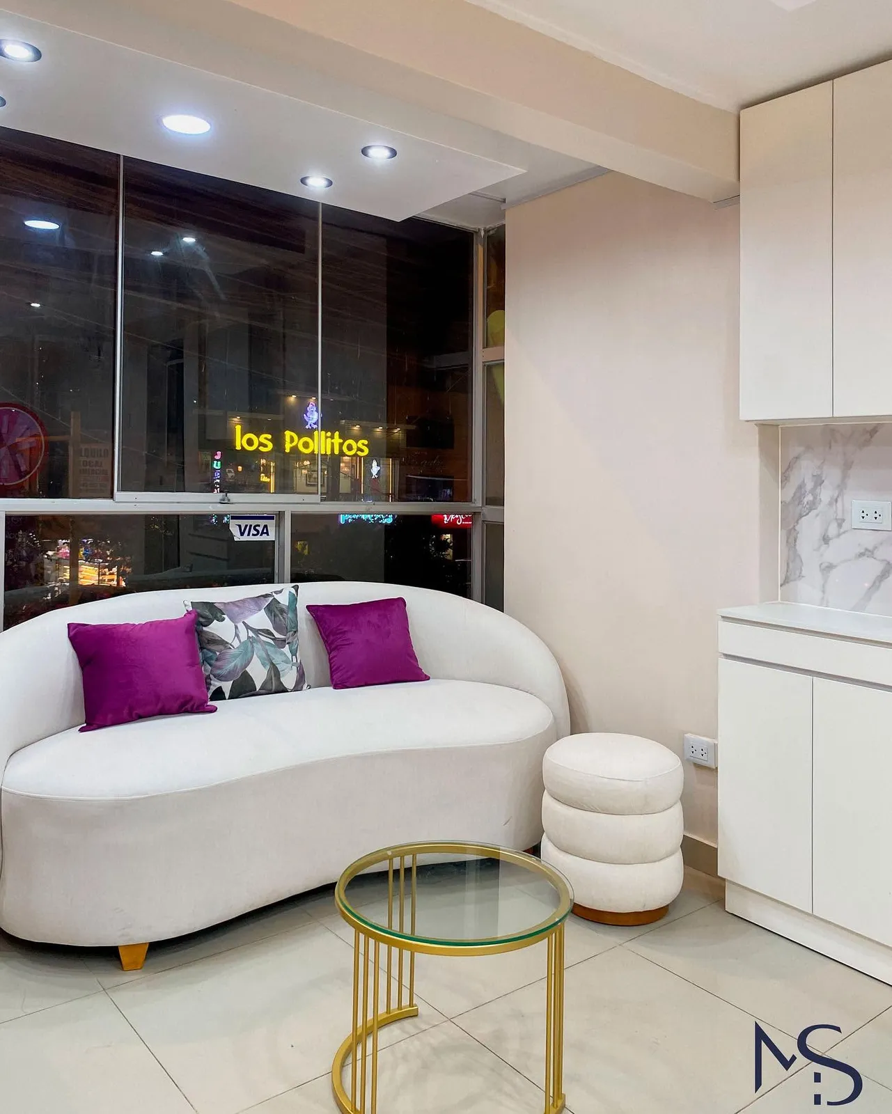 Zona de estar de la clínica con sofá curvo blanco, cojines morados, puff y mueble lacado blanco