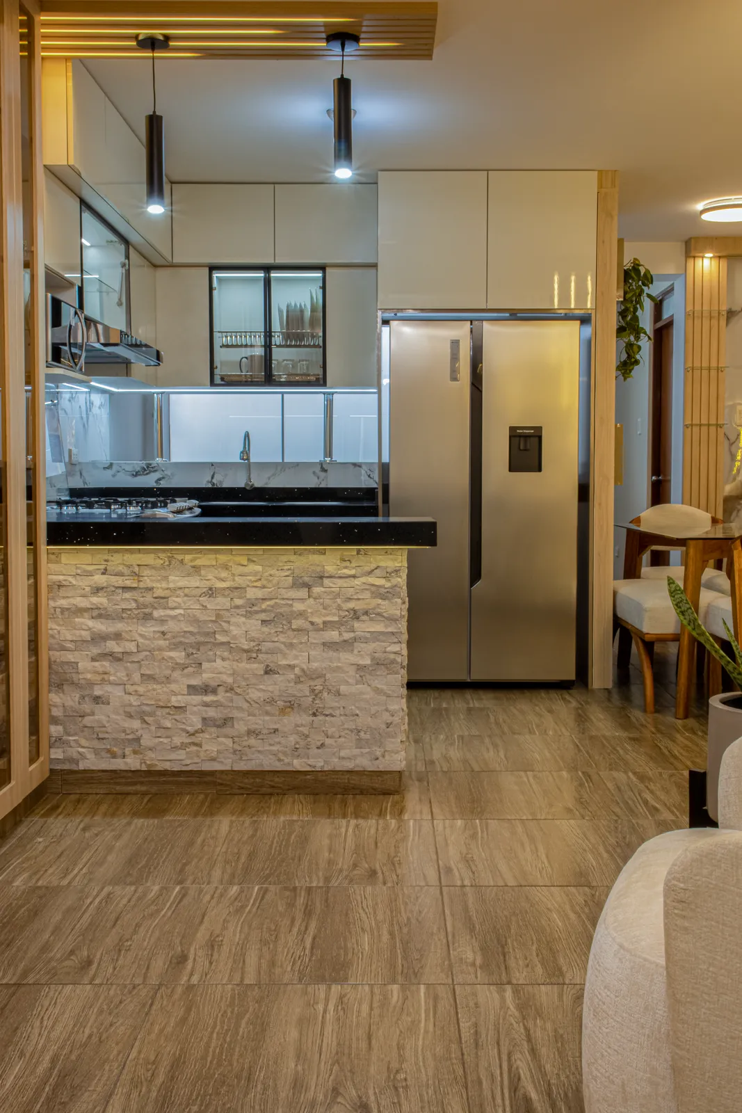 Cocina abierta con barra enchapada en piedra, muebles lacados blancos y lámparas colgantes negras