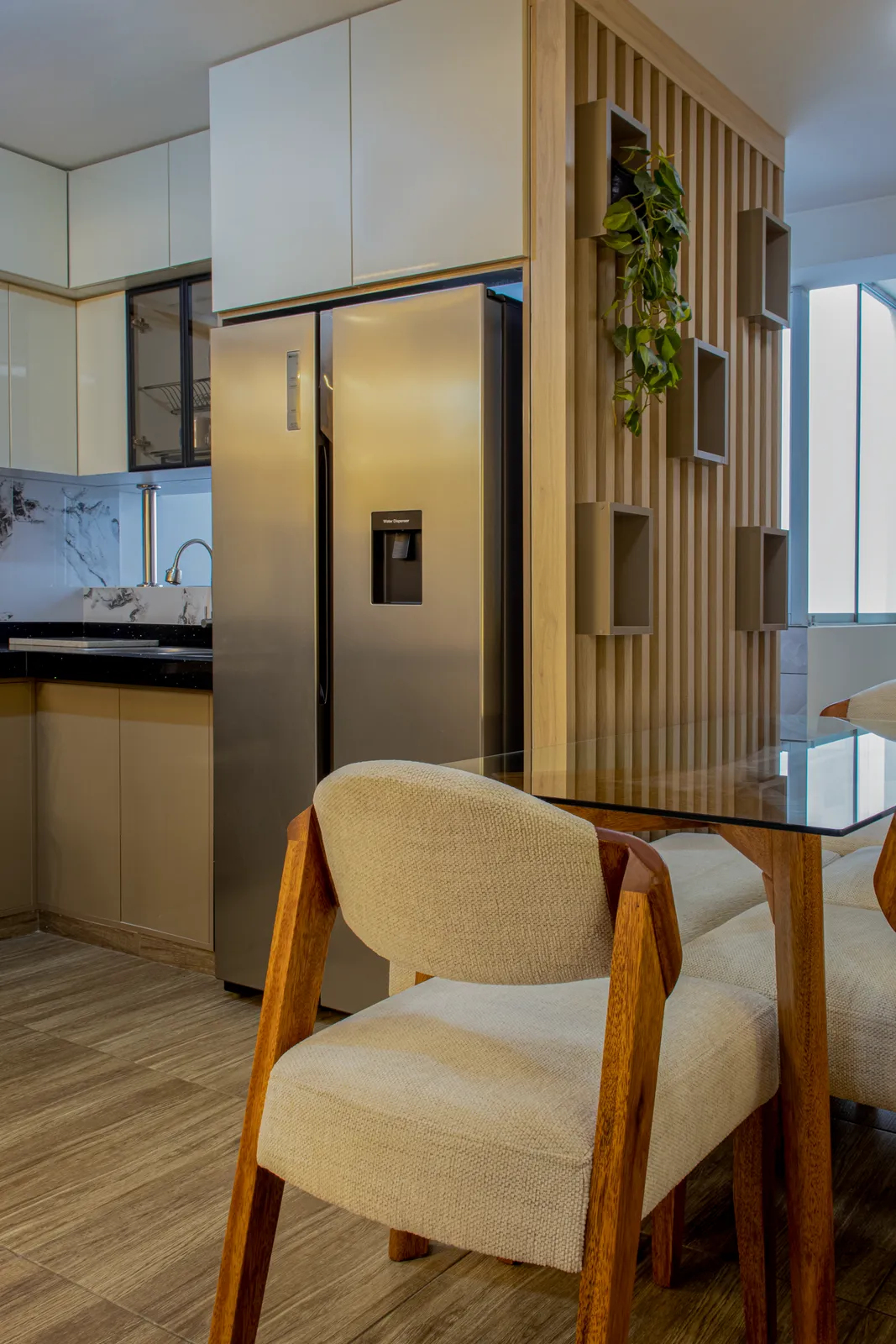 Comedor con sillas de madera y mesa de vidrio junto a una celosía de listones con nichos y plantas que separa la cocina — Santiago de Surco