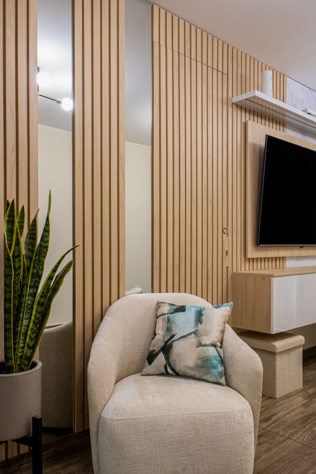 Sala con butaca de bouclé beige frente a un muro de listones de roble con televisor y sansevieria — Santiago de Surco