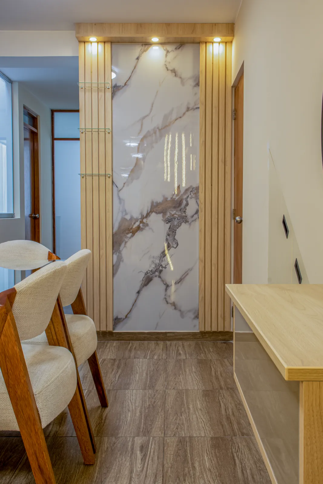 Detalle de un nicho de porcelanato efecto mármol blanco enmarcado por listones de roble con luz LED cálida — Santiago de Surco